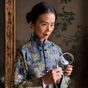 林若萱女士，传统丝织品鉴定专家，手持放大镜细察一匹十景缎的经纬结构，神情专注